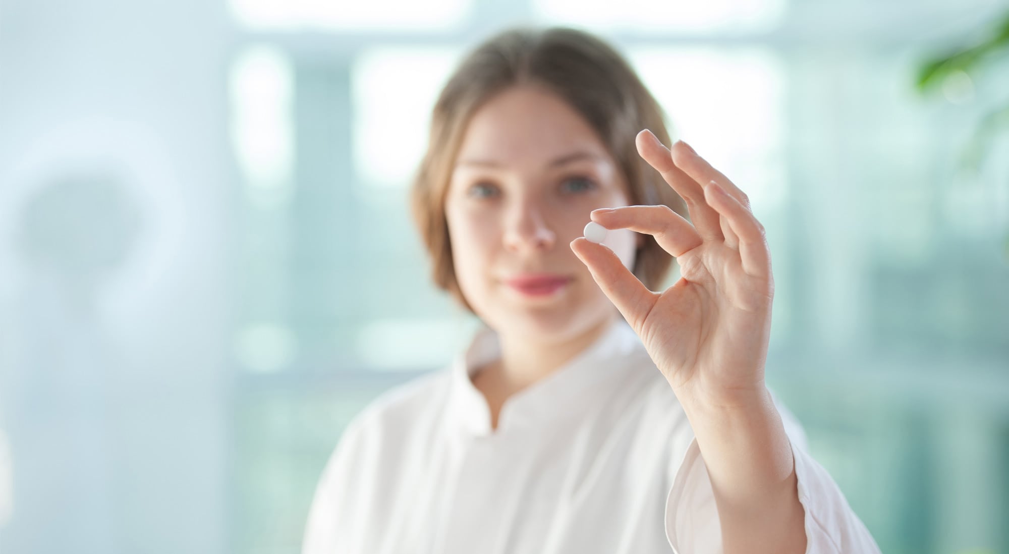 Ein Bild, das eine weibliche Person mit einer Tablette zwischen den Fingern zeigt.